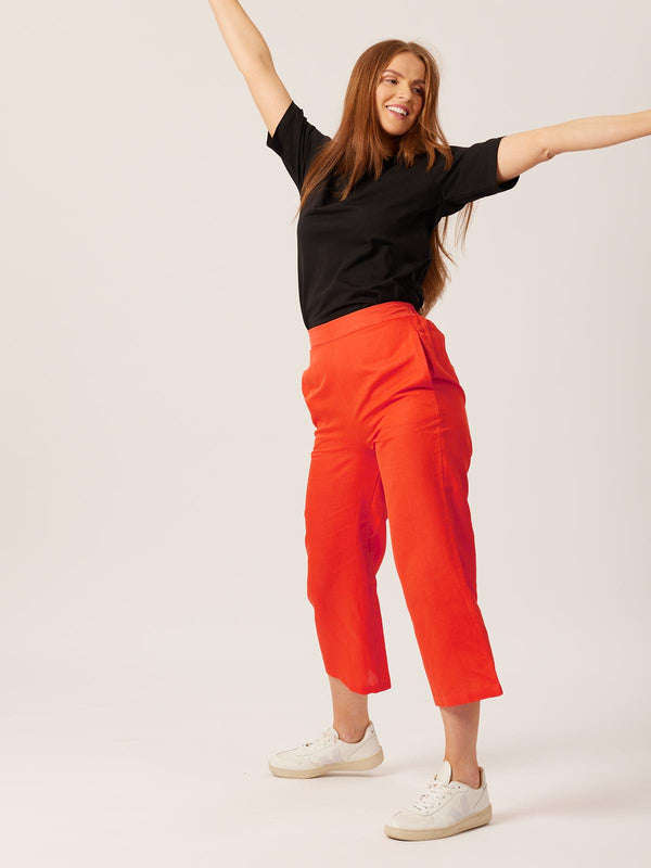 A model wears the Gigi trousers with the Penny t-shirt in black. They are pictured against a white backdrop with their arms outstretched in a playful manner. 
