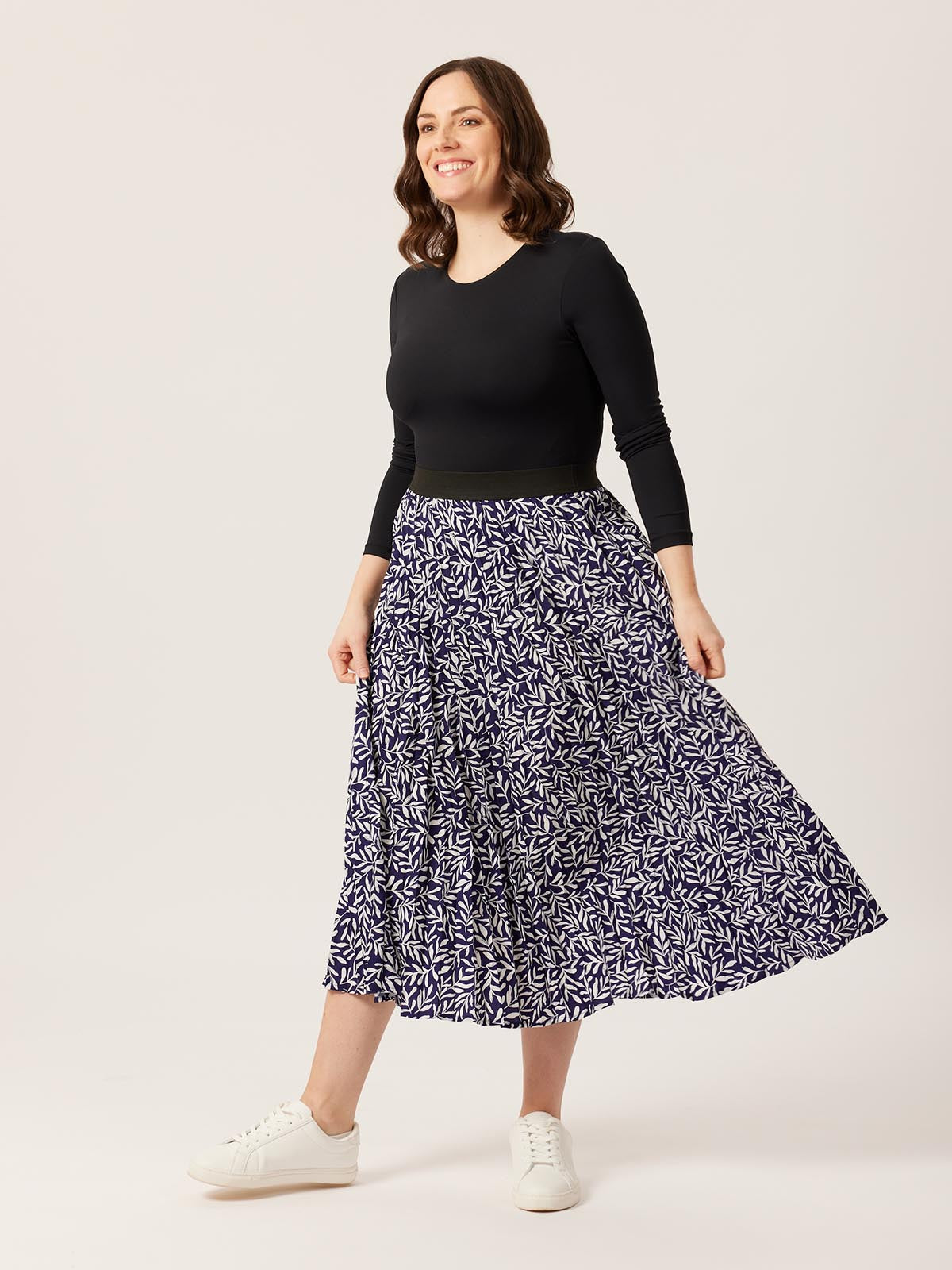 A model wearing the Gill skirt in navy with a long sleeve back top, pictured on a white background and smiling. 