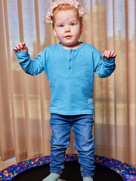 A child wearing the Harris sustainable kids pique t-shirt in blue, pictured jumping on a mini trampoline with their arms raised. 