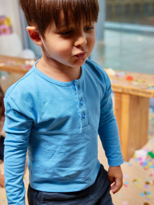 A child wearing the Harris sustainable kids pique t-shirt in blue, pictured in a room with confetti on the floor in a party atmosphere. 