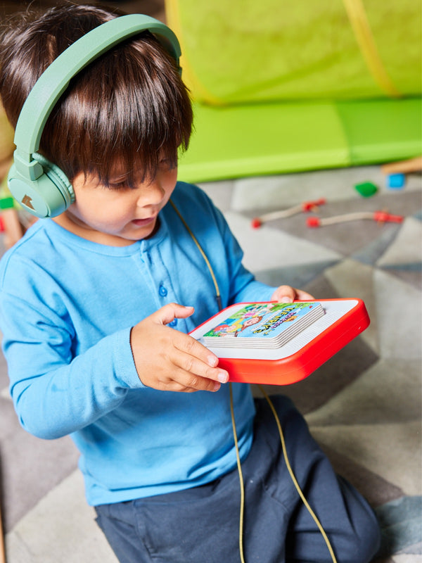 A child wearing the Harris sustainable kids pique t-shirt in blue, pictured on the floor with headphones on and looking at an audiobook player. 