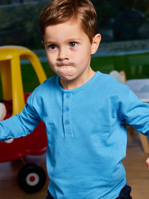 A child wearing the Harris sustainable kids pique t-shirt in blue, pictured in a playroom with their arms raised.