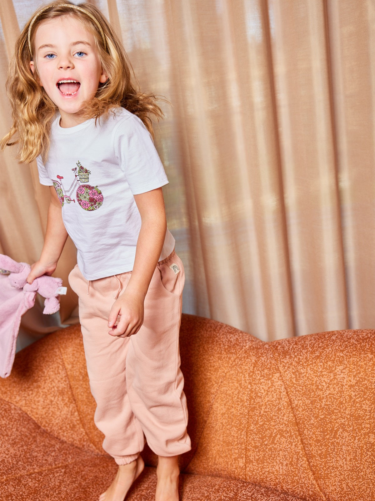 A child wearing the Ivy eco-friendly kids t-shirt with a multicolour bicycle print, pictured jumping on a couch. 