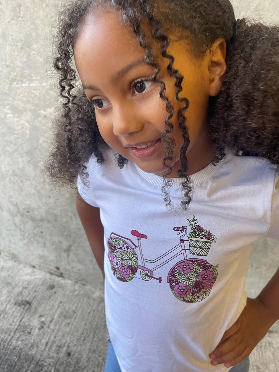 A closeup of a smiling child wearing the Ivy eco-friendly kids t-shirt with a multicolour bicycle print on a white cotton tee