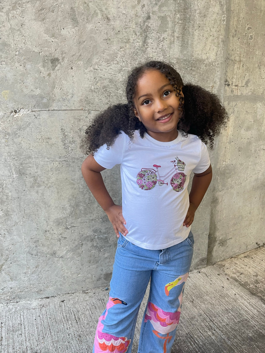 A child wearing the Ivy eco-friendly kids t-shirt with a multicolour bicycle print pictured smiling in front of a grey wall