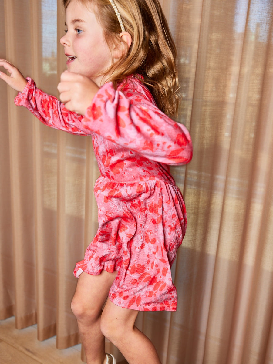 A child wearing the Izzy eco-friendly kids smock dress in pink, pictured mid-jump.