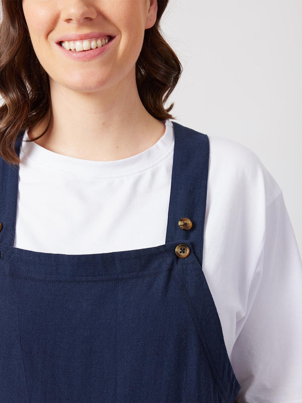 A close up of the sustainable Kathleen dungarees in navy, with a focus on the adjustable buttons on the shoulder fastening. 