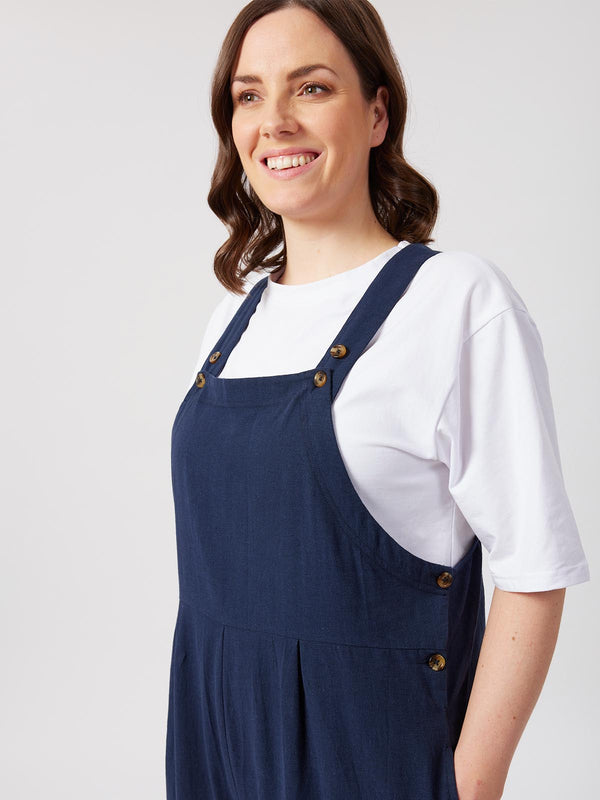 A model wears the Kathleen dungarees in navy, layered over a white short sleeved t-shirt, pictured against a while backdrop. 
