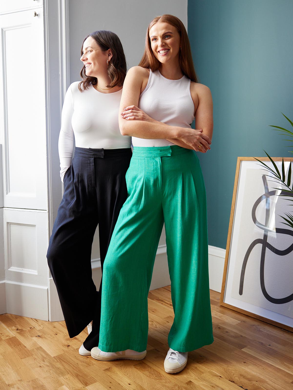 Two models, both wearing the Lana trousers - one in black and the other in green. Both models are smiling and looking in different directions. 