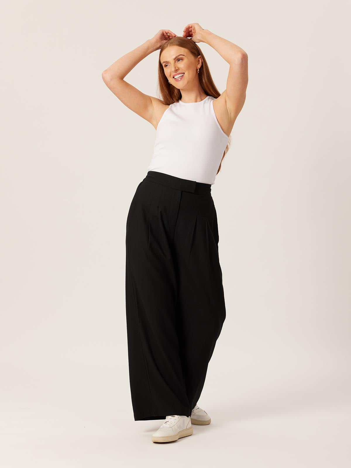 Model wearing the Lana sustainable trousers in black, pictured with their hands held above their head and smiling into the distance.