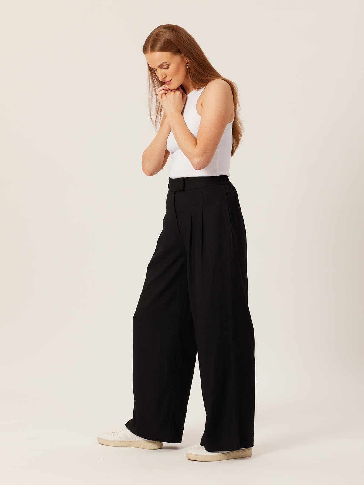 Model wearing the Lana sustainable trousers in black, pictured with their hands clasped and looking down at the ground.
