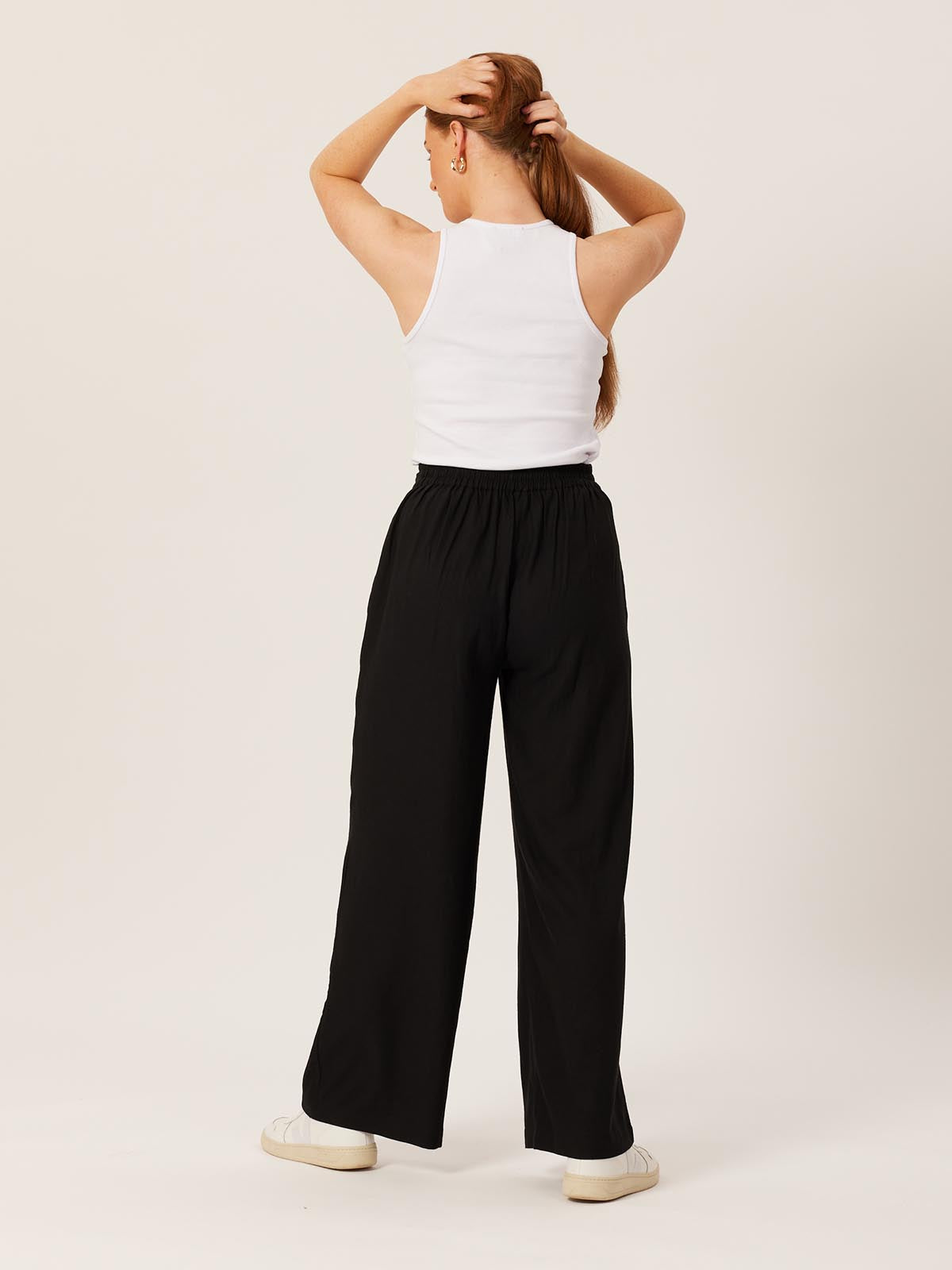 Model wearing the Lana sustainable trousers in black, pictured from the back pulling their hair to one side