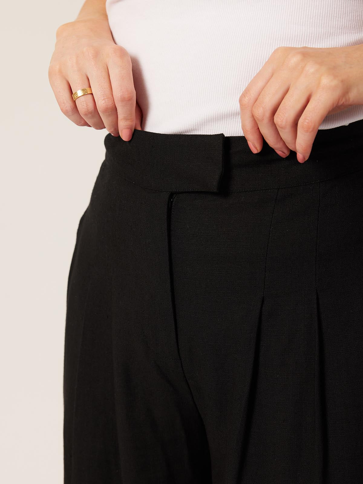 A close up shot of a model wearing the Lana trousers in black, displaying the zip and clasp fastening. 