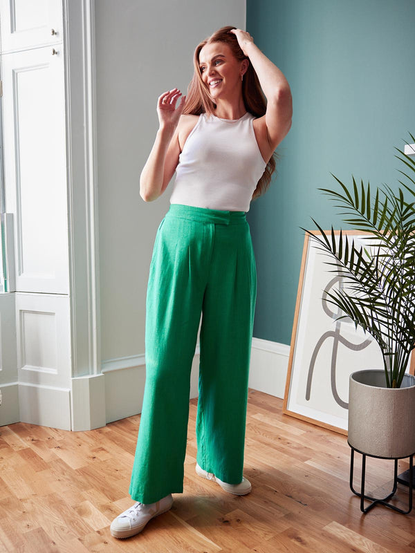 Model wearing the green Lana trousers and a white vest top, pictured smiling and running their hand through their hair.  
