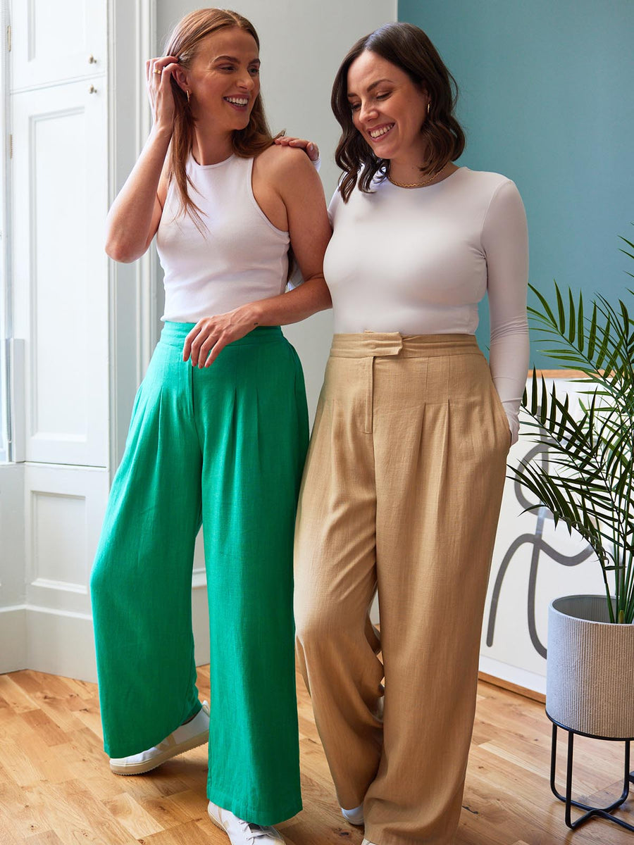 Two models, both wearing the Lana trousers - one in sand and the other in green. Both models are smiling and looking in different directions.