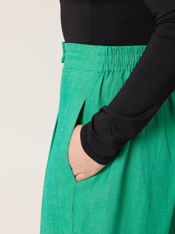 A close up of a model wearing the Lana green sustainable trousers, with their hands in one of the pockets and a long sleeve black t-shirt tucked in to the trousers.