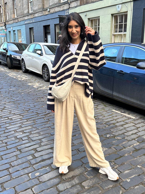 A model wearing the sustainable Lana trousers in sand, pictured looking into the camera and smiling. 