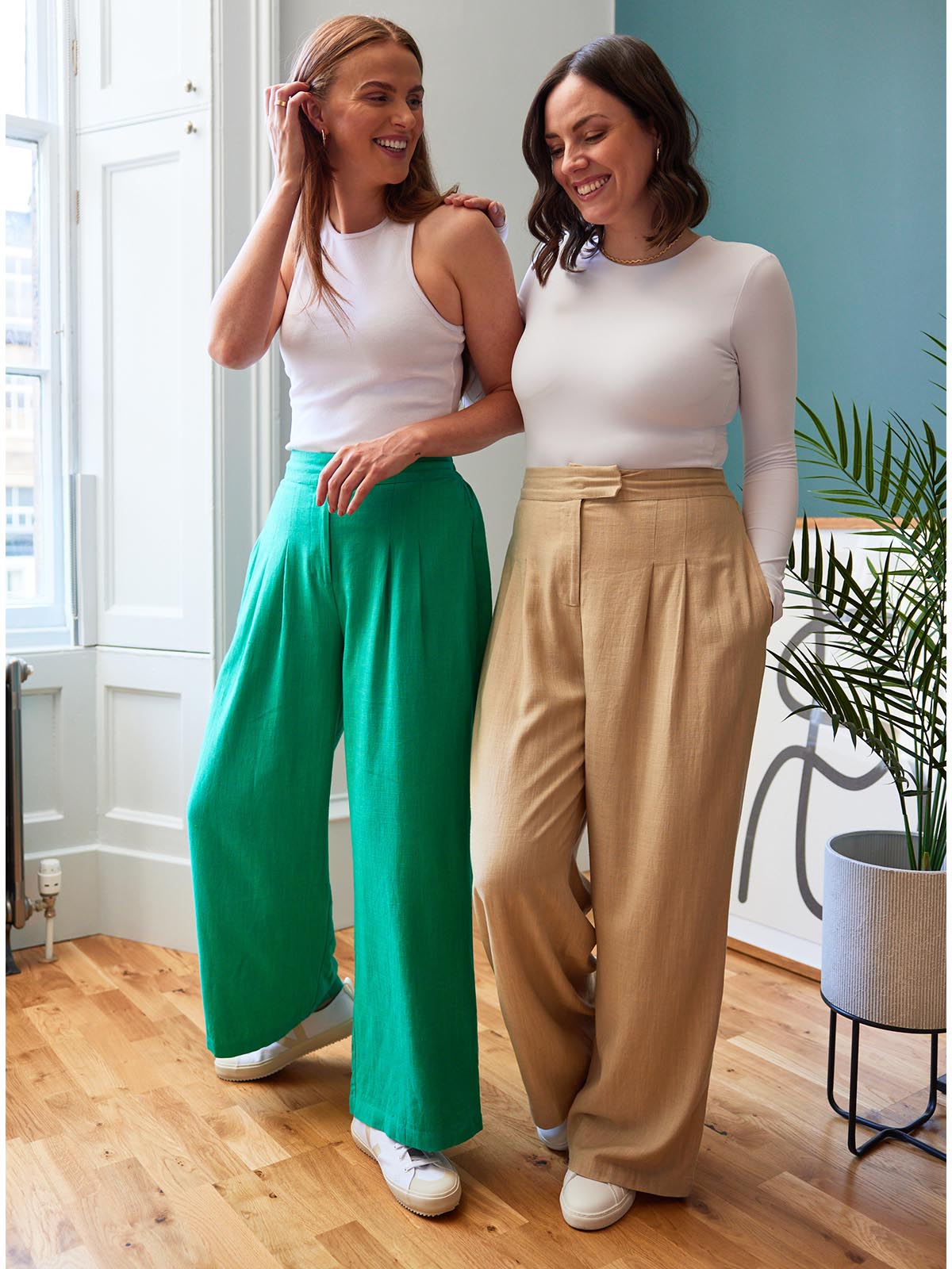 Two models, both wearing the Lana trousers - one in sand and the other in green. Both models are smiling and looking in different directions.