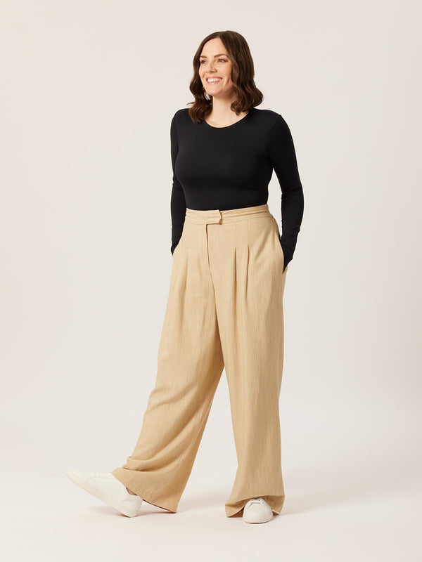 A model wearing the Lana trousers in sand, pictured on a white background with their hands in their pockets.