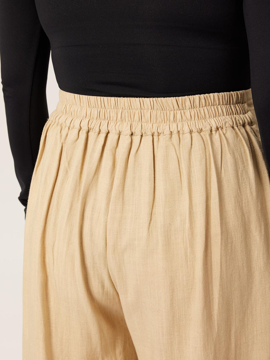 A close up of the back of a model wearing the Lana trousers in sand, with a focus on the elasticated waistband. 