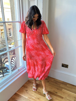 A model wearing the eco-friendly Lauren midi dress, pictured standing in front of a large window in a well lit room. 