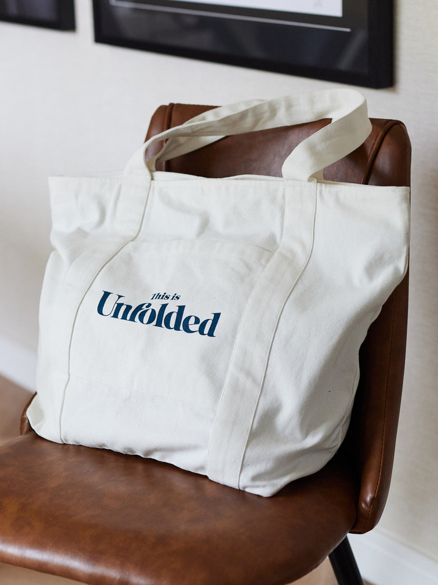 A Joey bag is pictured placed on a brown chair in a room with picture frames on the wall. 