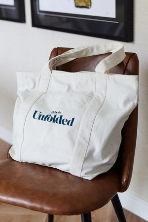 A Joey bag is pictured placed on a brown chair in a room with picture frames on the wall. 