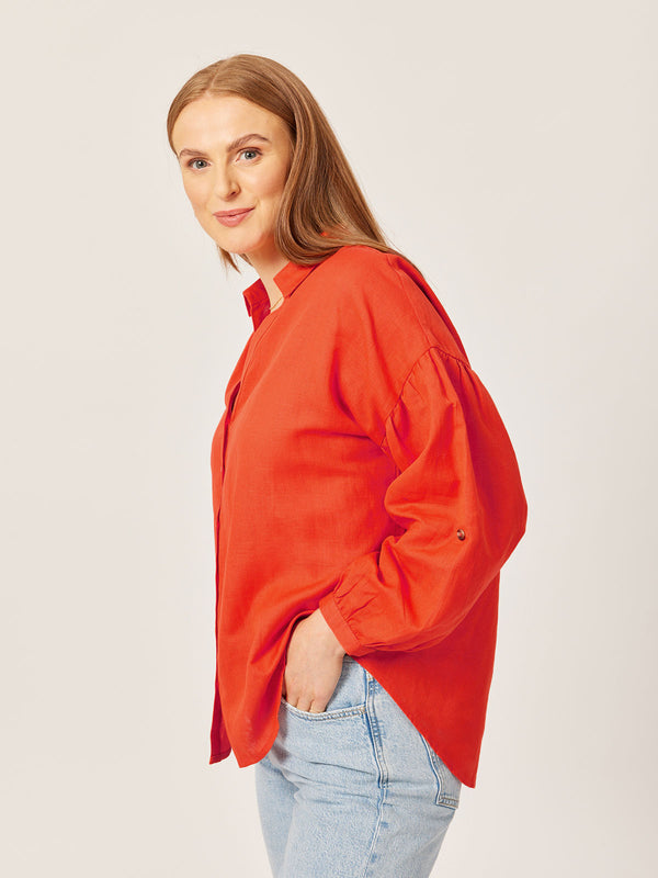 A model wears the Martha oversized shirt in red, pictured with one hand in their jeans pocket and smiling at the camera. 
