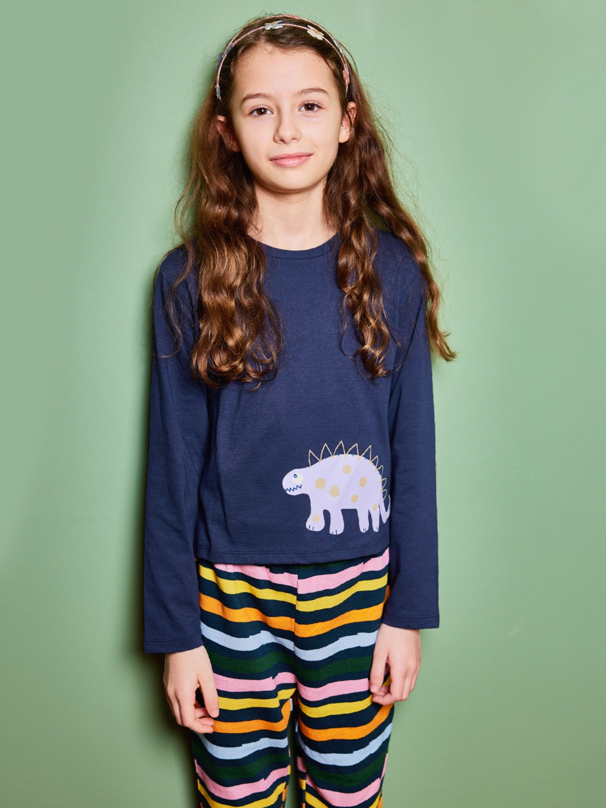 Child wearing the Melodi sustainable long sleeved kids t-shirt in navy blue with a dinosaur print, pictured looking straight into the camera and smiling. 