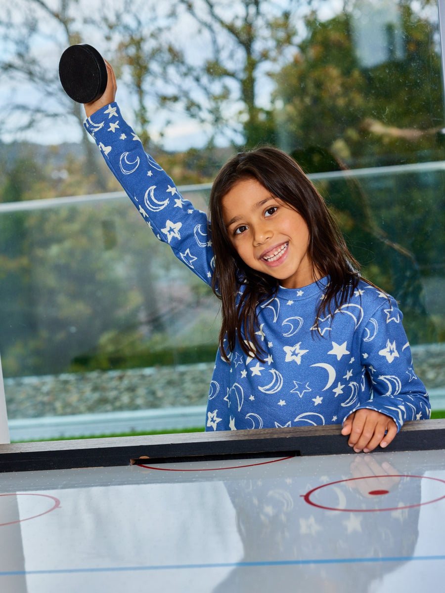 A child wearing the Mira sustainable kids PJ top in blue with a white moon and star print, pictured playing a tabletop game. 