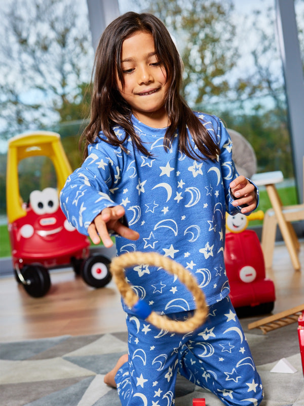 A child wearing the Mira sustainable kids PJ set in blue with a white moon and star print, pictured in a playroom throwing a rope toy. 