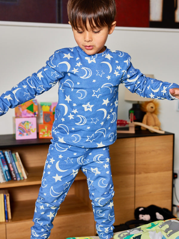 A child wearing the Mira sustainable kids PJ set in blue with a white moon and star print, pictured jumping on a bed. 