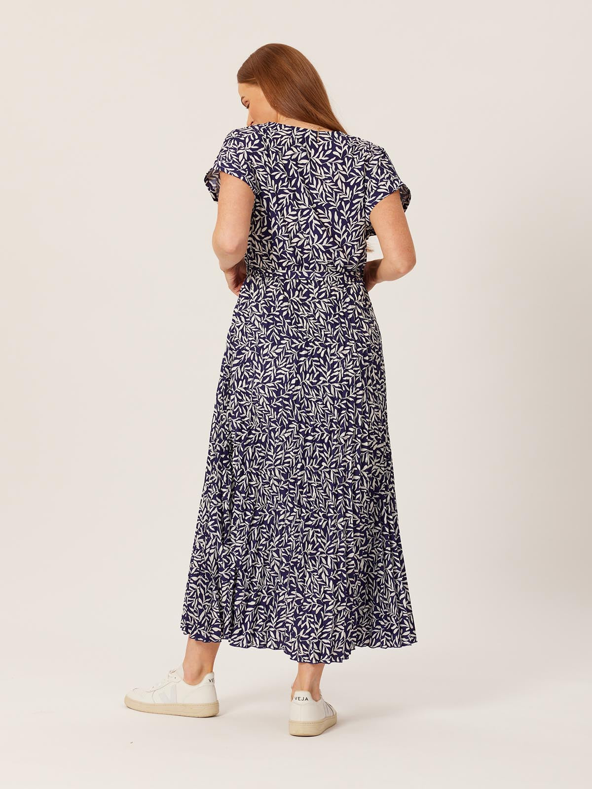 A model wears the Nena wrap dress and is pictured from behind against a white background. Their hair is pushed to one side and they are looking towards the ground. 