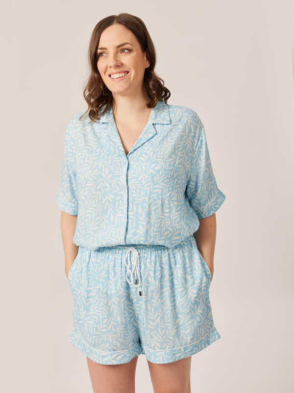 A model wears the Sian pyjama set in blue abstract leaf print. They are pictured smiling and looking into the distance.