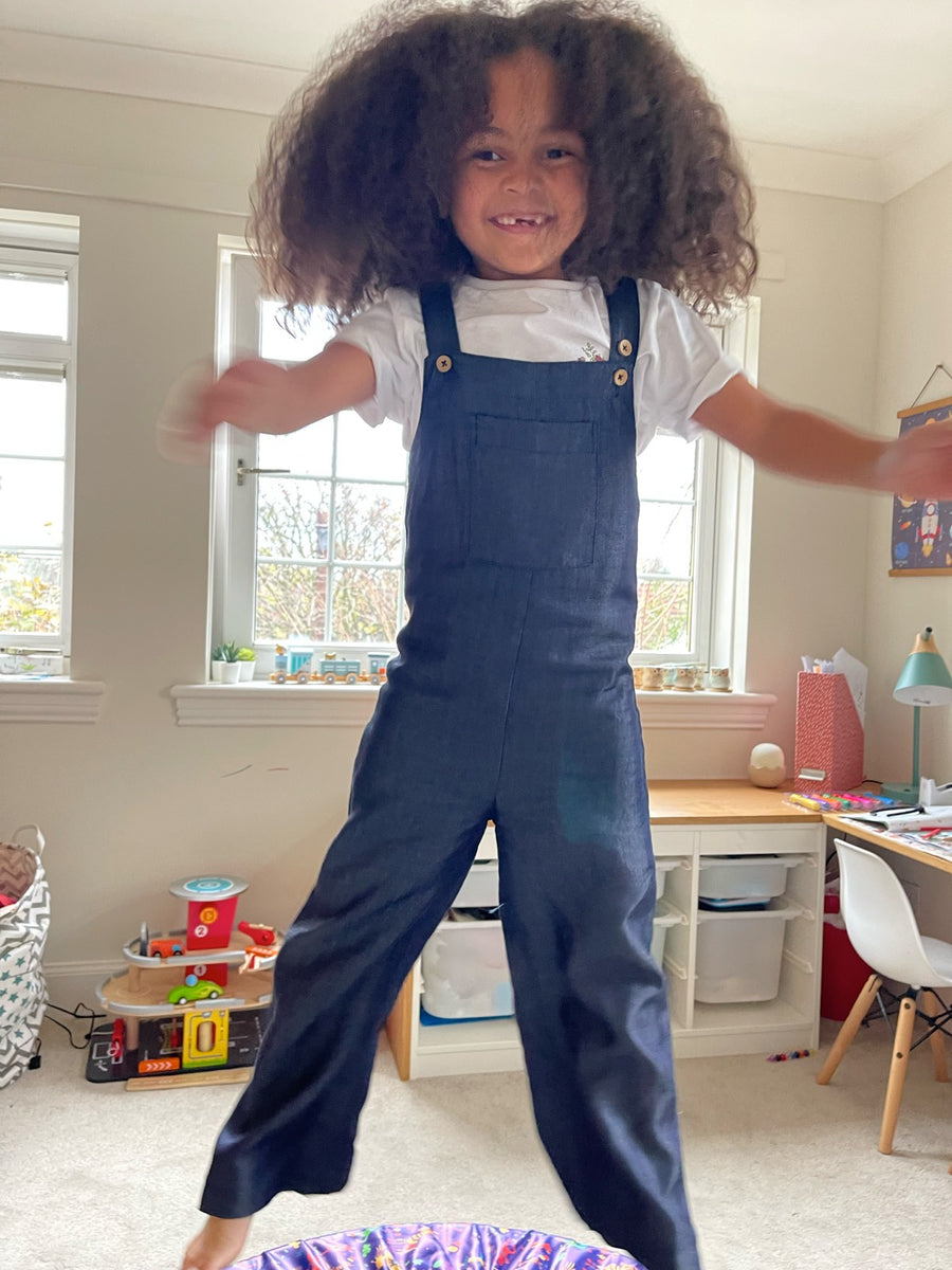 A child wearing the Sofia sustainable kids dungarees, pictured jumping on a mini trampoline. 